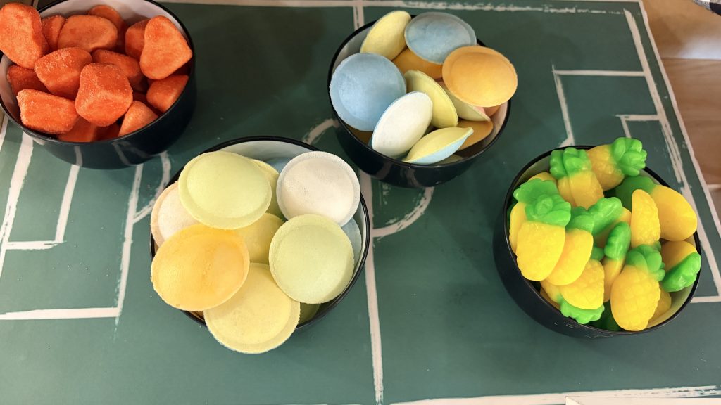 Mini recipientes de golosinas (negros) sobre campo de fútbol en porexpan